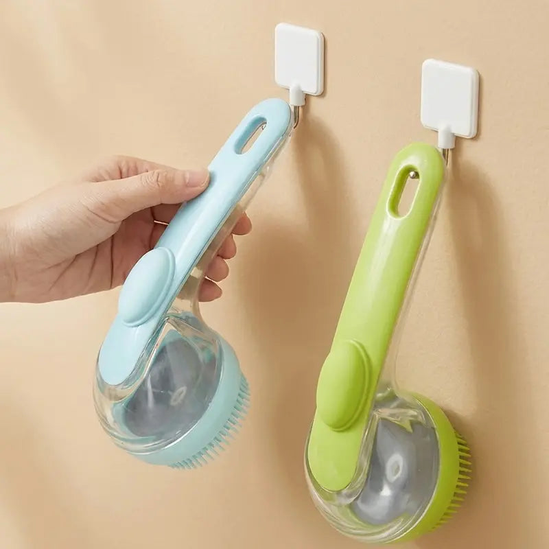 A hand holds a light blue Calivo™ Pet Bath & Grooming Brush with a shampoo dispenser, while an identical lime green one hangs on a hook beside it.